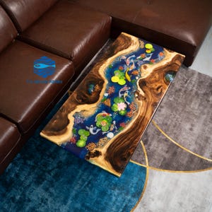 May include: A rectangular coffee table with a unique design. The table features a blue resin river with koi fish, lily pads, and other aquatic elements. The table's edges are made of natural wood, creating a striking contrast.