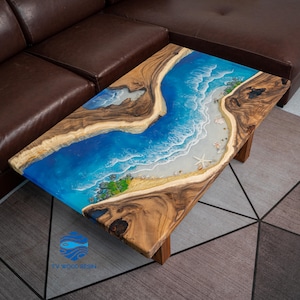 Könnte beinhalten: Rechteckiger Couchtisch mit Strandmotiv. Der Tisch hat einen Holzrahmen und Beine, mit einer Harzplatte, die einen blauen Ozean, weißen Sand und einen Seestern darstellt. Die Abmessungen des Tisches sind nicht sichtbar.