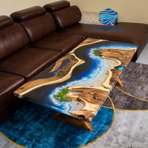 Puede incluir: Mesa de centro de madera hecha a mano con un diseño único de resina epoxi. La mesa presenta una escena de río y playa con detalles en azul, blanco y verde. La mesa está sostenida por patas de madera y se coloca sobre una alfombra azul y gris.