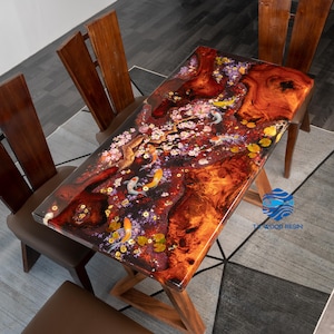 May include: Rectangular wooden table with a resin top featuring a koi pond design. The table has a natural wood grain base and a clear resin surface with koi fish, flowers, and lily pads. The table is surrounded by wooden chairs.