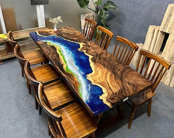 Op de afbeelding: Een grote houten eettafel met een blauwe en witte epoxyhars inlay die lijkt op een rivier of oceaan. De tafel is omringd door zes houten stoelen.