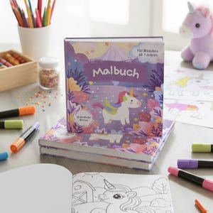 May include: A children's coloring book titled "Malbuch" with a unicorn illustration on the cover. The book is surrounded by coloring supplies, including markers and colored pencils. A plush unicorn toy is in the background.