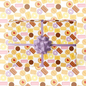 Könnte beinhalten: Ein Geschenk, das mit einem hellvioletten Band und einer Schleife verpackt ist. Das Geschenkpapier ist weiß und mit einem Muster aus verschiedenen Keksen bedeckt, darunter herzförmige, runde und rechteckige Kekse in Braun-, Gelb- und Rosatönen.