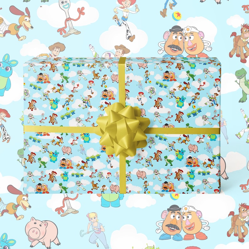 Puede incluir: Una caja de regalo envuelta con un fondo azul claro con un patr&oacute;n de personajes de Toy Story. La caja est&aacute; atada con una cinta dorada y un gran lazo dorado. Los personajes incluyen a Woody, Buzz Lightyear y Mr. Potato Head.