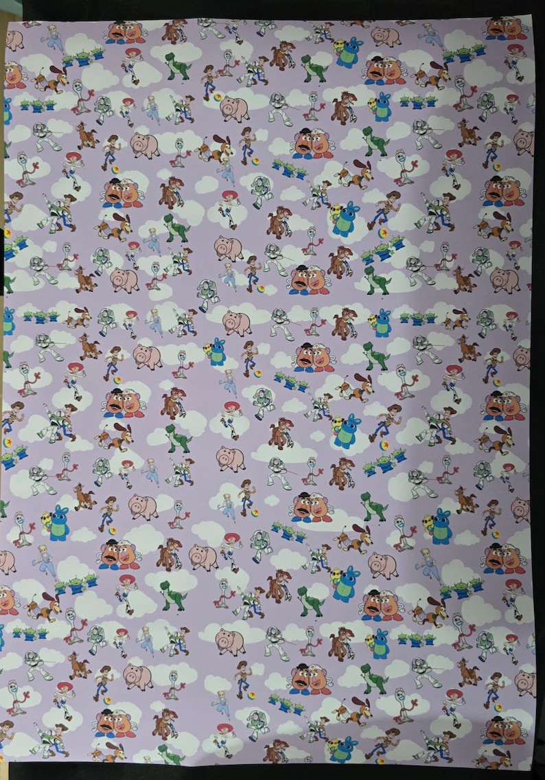 May include: A sheet of lavender-colored wrapping paper featuring a repeating pattern of cartoon characters, including a cowboy, a space ranger, a dinosaur, and a pig. White cloud shapes are interspersed throughout the design.