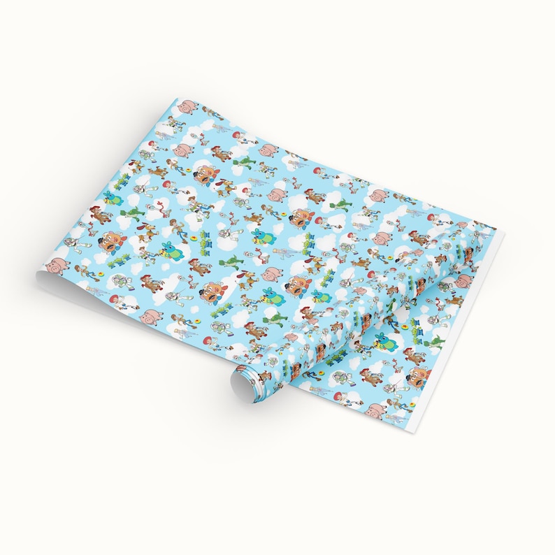 Puede incluir: Un rollo de papel de regalo azul claro con un patr&oacute;n repetido de personajes de dibujos animados, nubes y otros elementos. El papel est&aacute; parcialmente desenrollado, revelando el dise&ntilde;o. Los personajes son de varios colores.