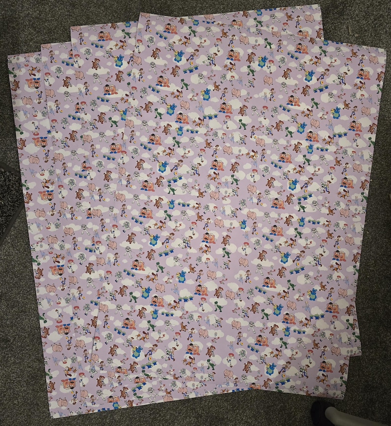 May include: Four sheets of patterned paper featuring a repeating design of cartoon characters, clouds, and other elements on a light purple background. The characters are in various poses and colors.