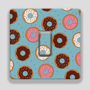 May include: A light switch cover featuring a pattern of colourful doughnuts and sprinkles on a light blue background.