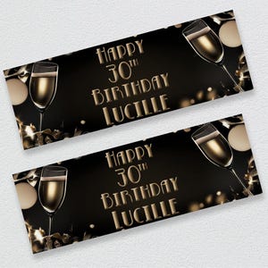 Op de afbeelding: Twee zwarte banners met gouden tekst en champagneglazen. De tekst luidt "Happy 30th Birthday Lucille" in een decoratief lettertype. De achtergrond bevat bokeh-lichten en linten.