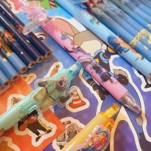 Op de afbeelding: Een verzameling Zootopia-thema vulpotloden en houten potloden. De vulpotloden hebben kleurrijke houders met karakterafbeeldingen en plastic clips. De houten potloden hebben donkerblauwe houders met sterpatronen en karakterprints.