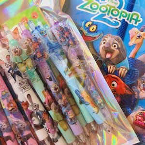 Op de afbeelding: Een set Zootopia 2 pennen verpakt in een holografisch plastic zakje. Elke pen is voorzien van kleurrijke karakterafbeeldingen uit de film, waaronder Judy Hopps en Nick Wilde, met doorzichtige plastic doppen en decoratieve opzetstukken.