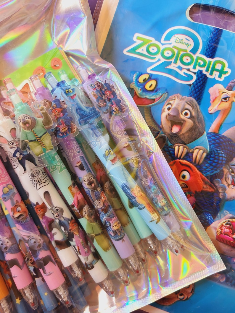 Op de afbeelding: Een set Zootopia 2 pennen verpakt in een holografisch plastic zakje. Elke pen is voorzien van kleurrijke karakterafbeeldingen uit de film, waaronder Judy Hopps en Nick Wilde, met doorzichtige plastic doppen en decoratieve opzetstukken.
