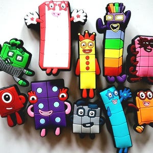 Puede incluir: Una colección de figuras de personajes de Numberblocks de colores. Las figuras son de varios colores, incluyendo rojo, verde, morado, amarillo y azul. Cada figura tiene un diseño y expresión únicos.