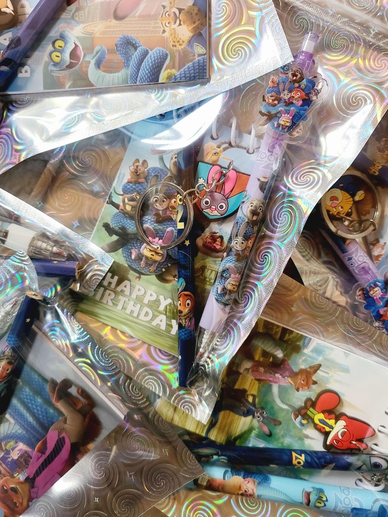May include: A collection of Zootropolis-themed stationery and accessories, including pens, keyrings, and stickers. The items are packaged in clear, iridescent cellophane. A keyring features Judy Hopps and Nick Wilde. Some items have "Happy Birthday" text.