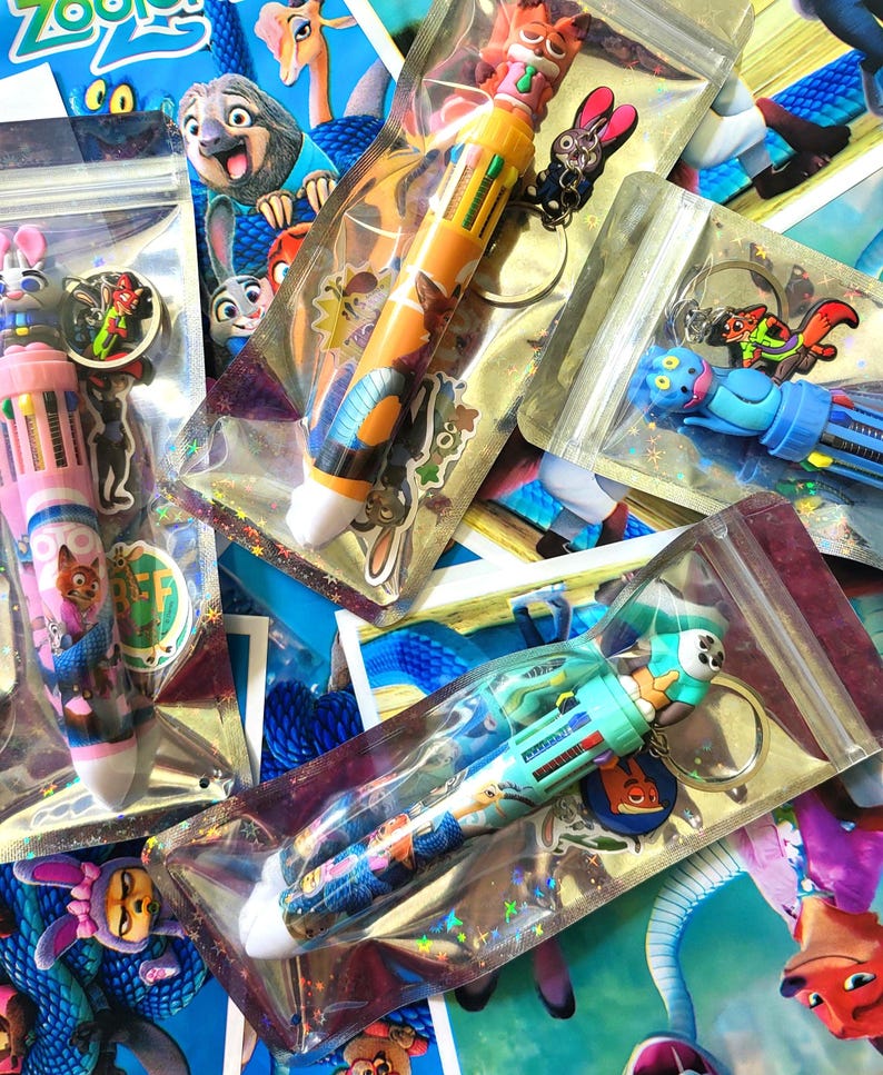 Pu&ograve; includere: Diverse penne multicolore con personaggi del film d'animazione "Zootropolis" sono esposte in confezioni di plastica trasparente. Ogni penna ha un personaggio diverso in cima e un portachiavi abbinato. Le penne sono in vari colori, tra cui rosa, blu e giallo.