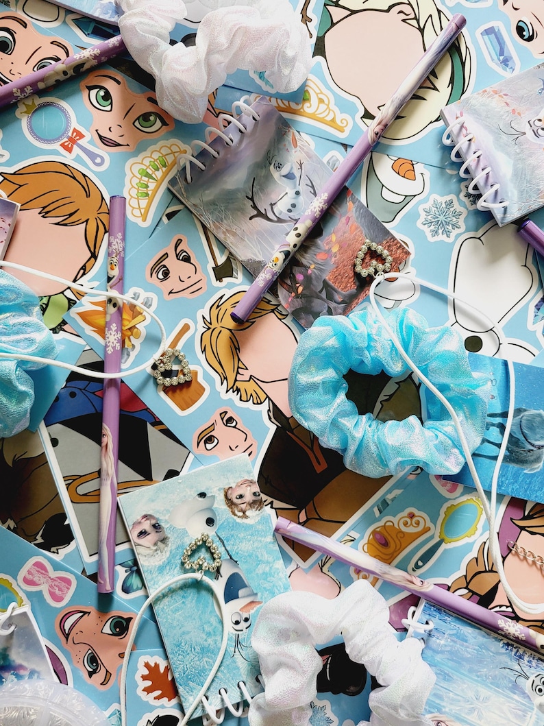 Peut inclure: Une collection de papeterie et d'accessoires sur le th&egrave;me de La Reine des Neiges comprenant des crayons violets &agrave; motifs de flocons, des petits carnets &agrave; spirales, des chouchous en tissu bleu et blanc, et des breloques en forme de c&oelig;ur.