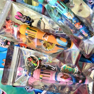 Pu&ograve; includere: Diverse penne multicolori con disegni di personaggi sono confezionate in sacchetti di plastica trasparente. Le penne hanno pi&ugrave; colori di inchiostro e sono decorate con personaggi dei cartoni animati. Alcuni sacchetti includono portachiavi di personaggi.