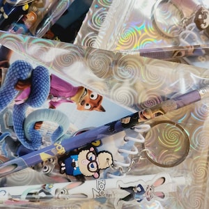 May include: A collection of Zootropolis-themed stationery and accessories. Includes pencils, keyrings, and a spiral notebook, all featuring characters like Nick Wilde and Judy Hopps. Items are packaged in clear plastic.