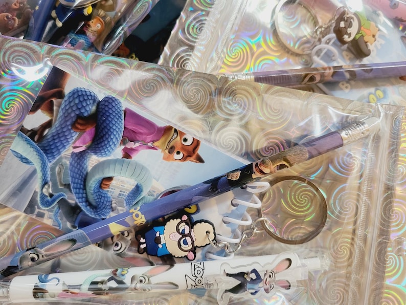 May include: A collection of Zootropolis-themed stationery and accessories. Includes pencils, keyrings, and a spiral notebook, all featuring characters like Nick Wilde and Judy Hopps. Items are packaged in clear plastic.