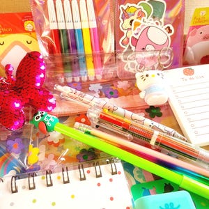 May include: A collection of colourful stationery items, including a set of six multi-coloured markers, a set of multi-coloured pens, a small notebook with a rainbow design, a green pen with a rainbow design, a pink butterfly sequin, a small blue notepad with a to-do list, and a variety of stickers and charms.