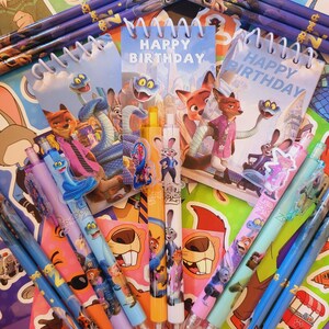 Op de afbeelding: Een collectie Zootopia-thema schrijfwaren, waaronder spiraalblokken met de tekst Happy Birthday, diverse pennen met karakter-toppers en potloden. De items zijn voorzien van kleurrijke illustraties van Nick Wilde, Judy Hopps en andere figuren.