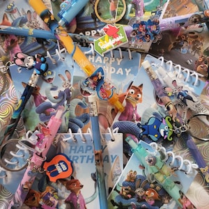 May include: A selection of Zootopia-themed stationery items, including pencils, keyrings, and small notebooks. The pencils have character toppers and colourful designs. The notebooks display "Happy Birthday". Keyrings with character designs are also present.