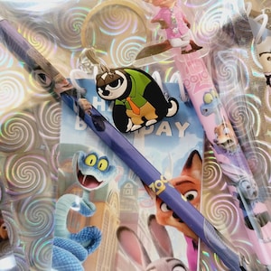 May include: A selection of Zootropolis-themed stationery, including pencils with character designs, a keyring, and a birthday card. The pencils feature characters such as Nick Wilde and Judy Hopps. The items are packaged in a clear, iridescent bag.