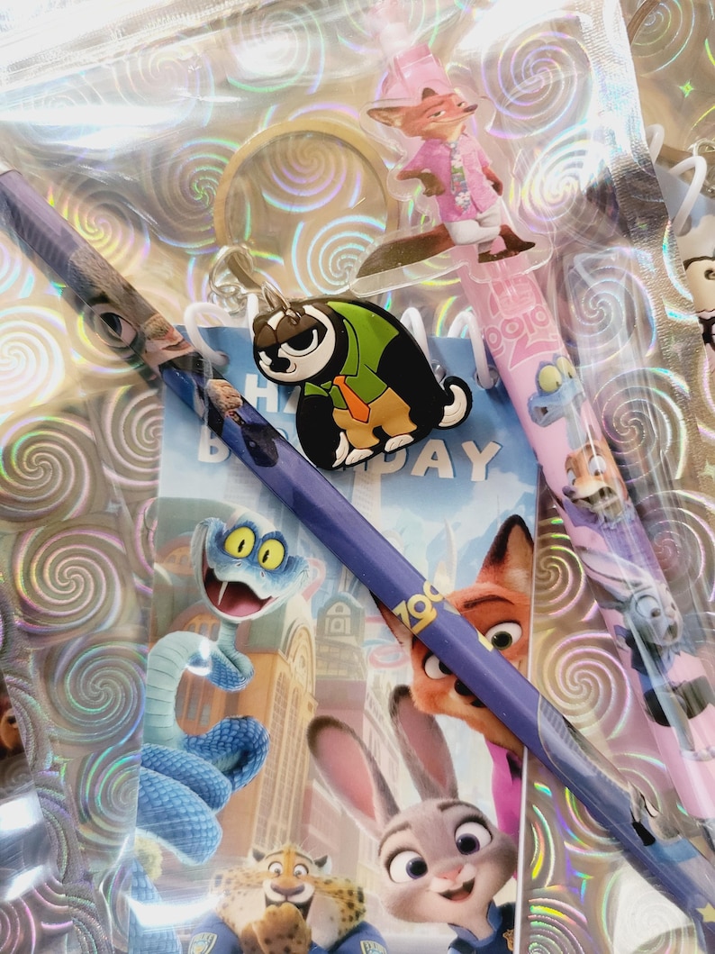 May include: A selection of Zootropolis-themed stationery, including pencils with character designs, a keyring, and a birthday card. The pencils feature characters such as Nick Wilde and Judy Hopps. The items are packaged in a clear, iridescent bag.