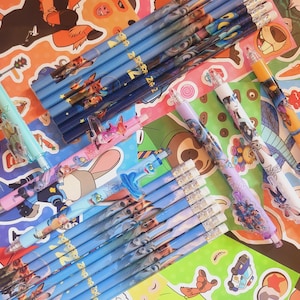 Op de afbeelding: Een verzameling Zootopia-schrijfinstrumenten, waaronder diverse blauwe houten potloden met karakterafbeeldingen, meerdere vulpotloden met kleurrijke plastic behuizingen en verschillende potloodtoppers met figuren.