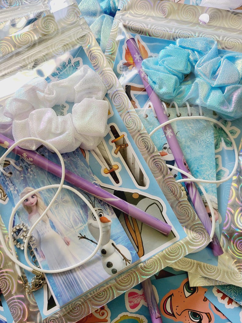 Peut inclure: Deux pochettes en plastique transparent contenant des kits de papeterie avec Elsa et Olaf de La Reine des Neiges. Chaque kit comprend un chouchou iris&eacute; blanc ou bleu clair, un crayon violet &agrave; motifs flocons, un collier cordon blanc et des autocollants.