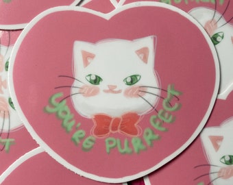 May include: A pink heart-shaped sticker with a white cat wearing a red bow tie. The text "You're purrfect" is written in green around the cat.