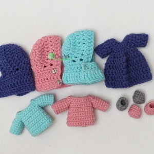 May include: A set of crocheted doll clothes in blue, pink and turquoise. The set includes a dress, two sweaters, two hooded jackets and four pairs of shoes.