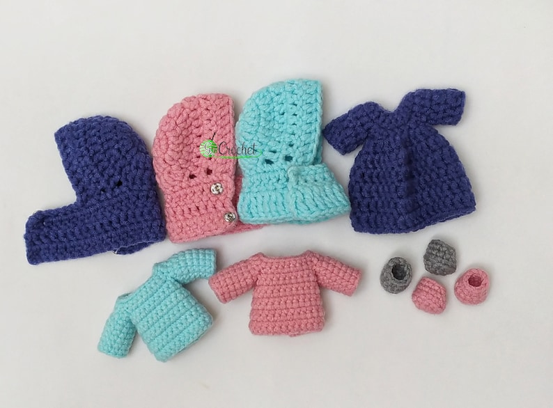 May include: A set of crocheted doll clothes in blue, pink and turquoise. The set includes a dress, two sweaters, two hooded jackets and four pairs of shoes.