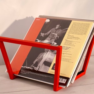 K&ouml;nnte beinhalten: Ein roter Metall-Plattenst&auml;nder mit einem Stapel Schallplatten. Die oberste Platte zeigt ein Schwarzwei&szlig;foto eines Mannes, der Bass spielt. Das Plattencover hat den Text "Johnny Hodges Album with Jon Jones".