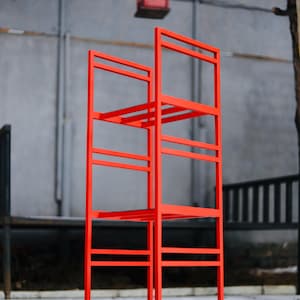 Könnte beinhalten: Ein leuchtend rotes Metallregal mit vier Regalböden. Das Regal steht auf einer schneebedeckten Oberfläche.