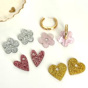 Peut inclure: Assortiment de boucles d'oreilles en forme de cœur et de fleur à paillettes. Les boucles d'oreilles sont en paillettes argentées, roses et dorées.