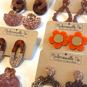 Peut inclure: Une collection de six paires de boucles d'oreilles présentées sur des cartes en carton brun étiquetées Mademoiselle No. Les boucles d'oreilles présentent diverses formes dont des cercles, ovales, gouttes et fleurs, en matériaux pailletés et unis.