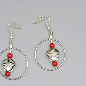 May include: Silver hoop earrings with red beads and a silver seashell charm.