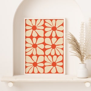 May include: A framed print with a geometric pattern of white flowers on a red background. The print is displayed on a white shelf with a vase of dried pampas grass.