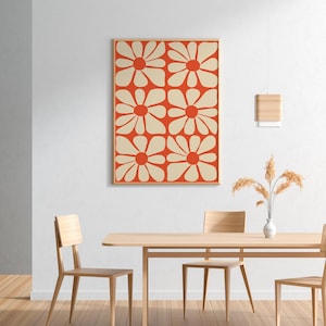 May include: A framed print of a geometric pattern featuring white flowers on a red background. The print is hanging on a white wall above a wooden table with two chairs.