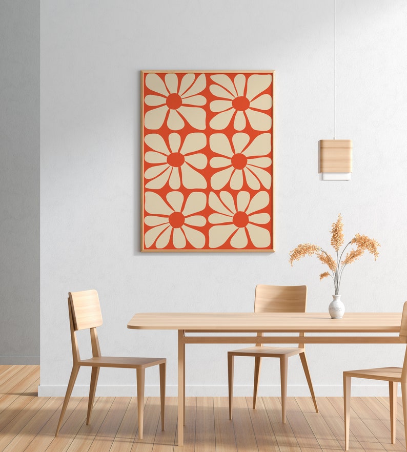 May include: A framed print of a geometric pattern featuring white flowers on a red background. The print is hanging on a white wall above a wooden table with two chairs.