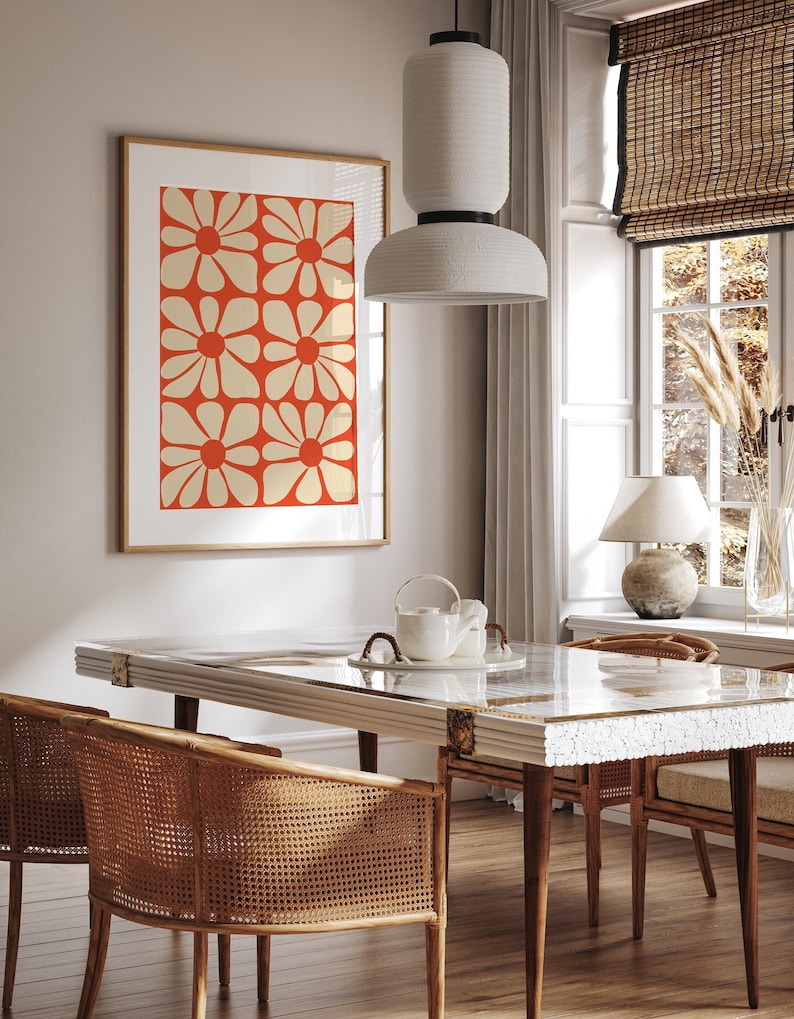 May include: A dining room with a white table with a white and gold mosaic top. The table has four chairs with woven cane seats and backs. A white pendant light hangs above the table. A framed print with a red background and white flowers hangs on the wall.