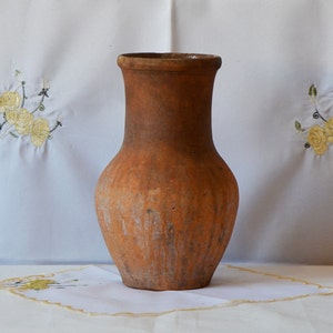 Op de afbeelding: Een terracotta vaas met een rond lichaam en een brede opening. De vaas heeft een rustieke, aardse uitstraling met een gevlekte bruine en oranje kleur.