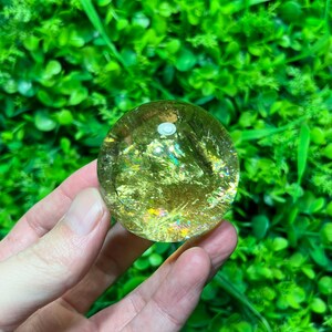 May include: A golden sphere with iridescent inclusions, a crystal ball with a smooth, polished surface.
