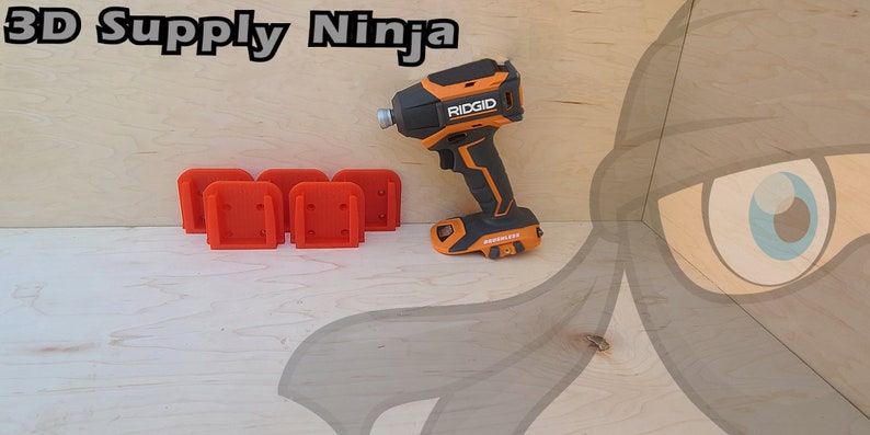 Pu&ograve; includere: Quattro supporti a parete arancioni stampati in 3D per un trapano, accanto a un trapano Ridgid nero e arancione su una superficie in legno. Lo sfondo &egrave; un viso di ninja dei cartoni animati.