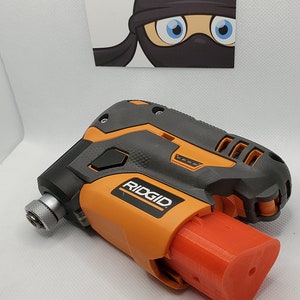 Puede incluir: Un taladro inal&aacute;mbrico negro y naranja con una bater&iacute;a roja. El taladro tiene el logotipo de RIDGID en el lateral.