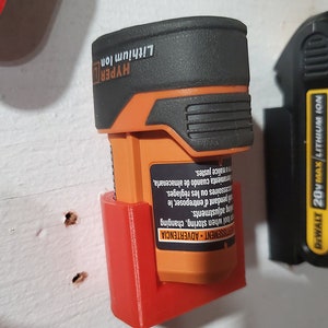 May include: A red plastic wall mount for a battery charger. The charger is orange and black and says "HYPER Lithium Ion". A black and yellow battery charger says "DEWALT 20V MAX Lithium Ion".