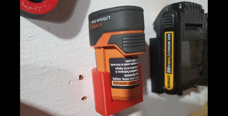May include: A red plastic wall mount for a battery charger. The charger is orange and black and says "HYPER Lithium Ion". A black and yellow battery charger says "DEWALT 20V MAX Lithium Ion".