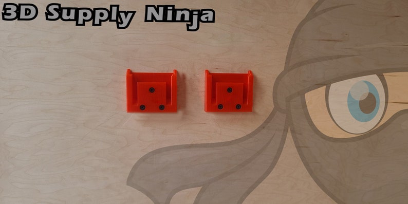 May include: Two bright orange plastic wall mounts with four black screw holes each. The mounts are attached to a light wood surface with a cartoon ninja illustration.