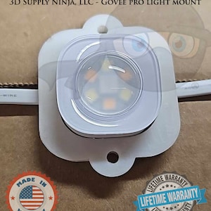 Puede incluir: Soporte de luz de plástico blanco con una cúpula transparente y seis luces LED en el interior. El soporte tiene un agujero para colgar y una etiqueta que dice "GARANTÍA DE POR VIDA".